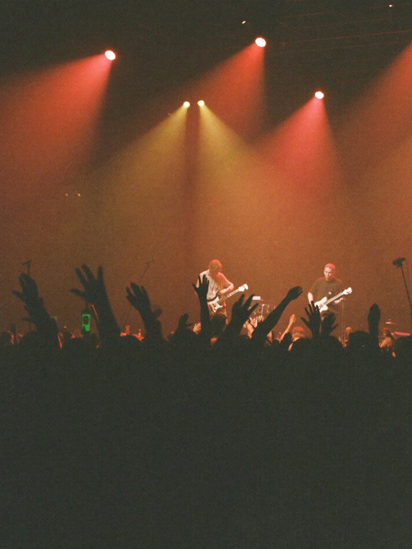 A band on a small stage under warm haze, seen from the crowd
